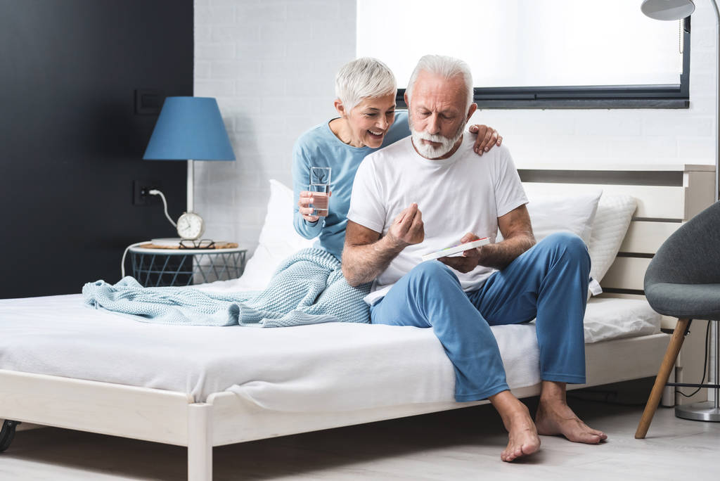 Evde yaşlı bir çift, yaşlı gri saçlı bir erkek ve kadın. Sağlık hizmetleri için ilaç alıyorlar. Yatakta otururken konsept bir çift vitamin alıyor. - Fotoğraf, Görsel