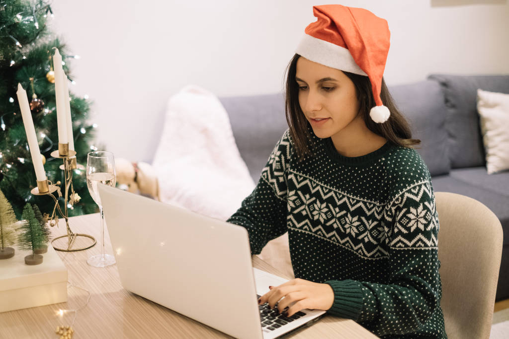 Mulher bonita com chapéu de Papai Noel sentado na frente de um laptop
 - Foto, Imagem