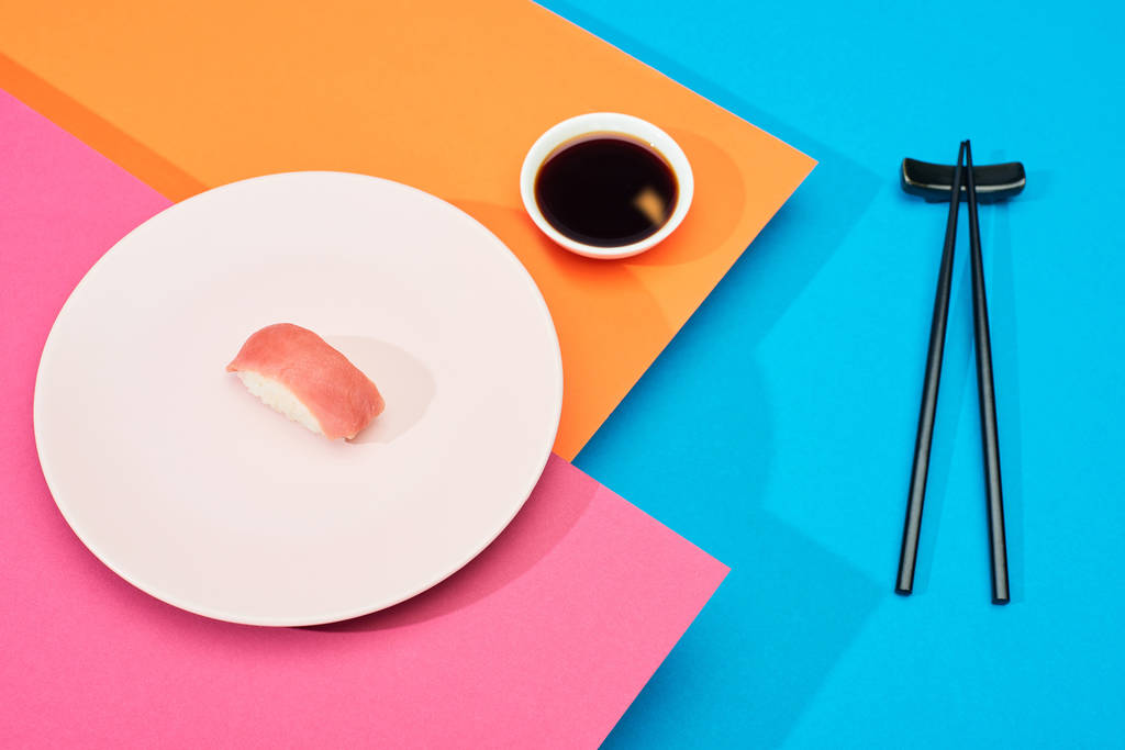 świeże nigiri z tuńczykiem w pobliżu sosu sojowego i pałeczki na różowej, niebieskiej, pomarańczowej powierzchni - Zdjęcie, obraz