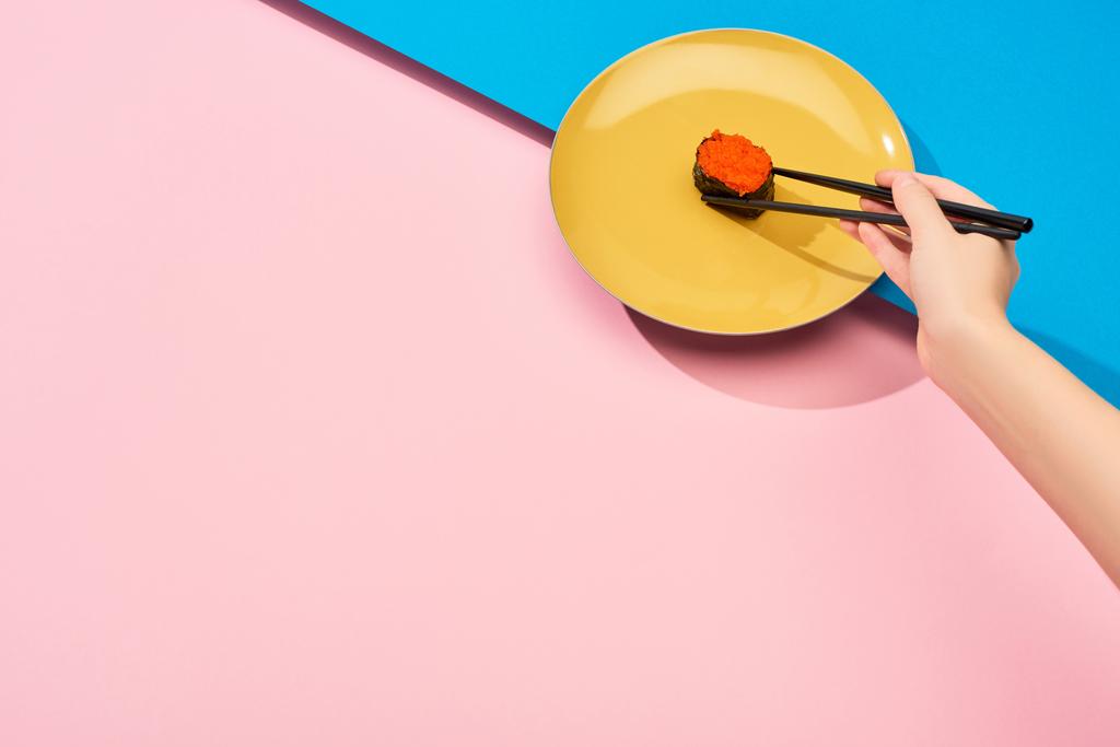 cropped view of woman eating fresh nigiri with red caviar with chopsticks on blue, pink surface - 写真・画像