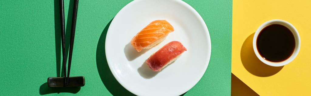 top view of fresh nigiri with salmon and tuna near soy sauce and chopsticks on green and yellow surface, panoramic shot - Photo, Image