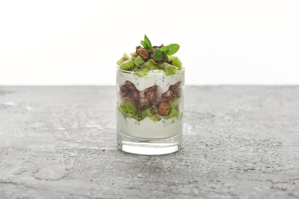 verse granola met kiwi en yoghurt in glas op grijs betonnen oppervlak geïsoleerd op wit - Foto, afbeelding