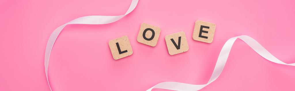 top view of curved ribbon and wooden blocks with love lettering isolated on pink, panoramic shot - Photo, Image