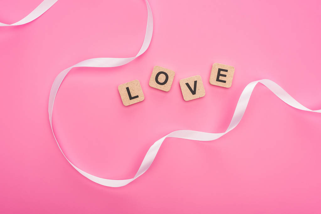 Draufsicht auf gebogenes Band und Holzklötze mit Liebesschrift isoliert auf rosa - Foto, Bild