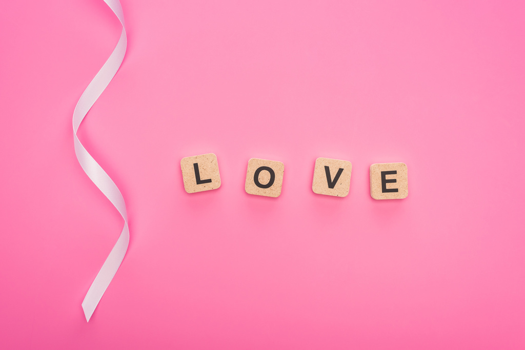 ピンクに孤立した愛の文字が刻まれた曲線のリボンと木のブロックのトップビュー - 写真・画像