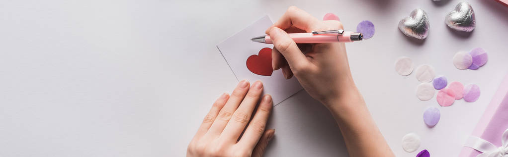 oříznutý pohled na ženu psaní na valentines karty se srdcem na bílém pozadí, panoramatický záběr - Fotografie, Obrázek