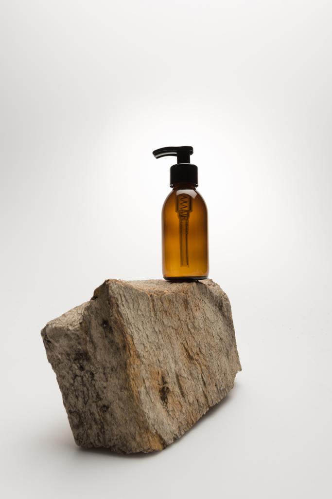 beyaz zemin üzerinde taştan yapılmış kozmetik şişe ve arka plan ışığı - Fotoğraf, Görsel