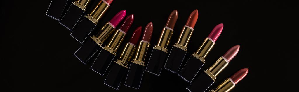 bovenaanzicht van diverse lippenstiften in luxe buizen geïsoleerd op zwart, panoramisch shot - Foto, afbeelding