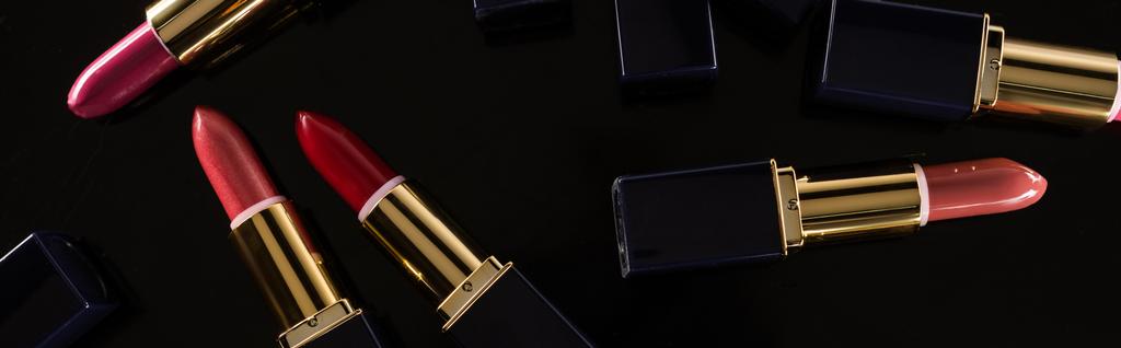 Draufsicht auf verschiedene Lippenstifte in Luxusröhrchen vereinzelt auf schwarzen, panoramischen Aufnahmen - Foto, Bild