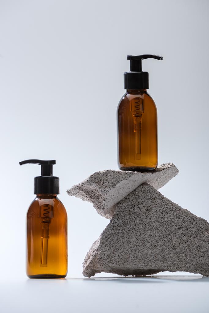 dispenser cosmetische flessen met stenen op witte achtergrond met achtergrondverlichting - Foto, afbeelding