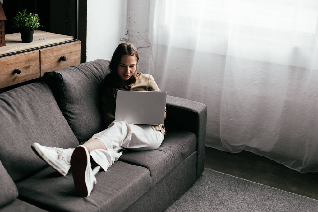 Selective focus of young woman with prosthetic leg using laptop on sofa at home - Photo, Image