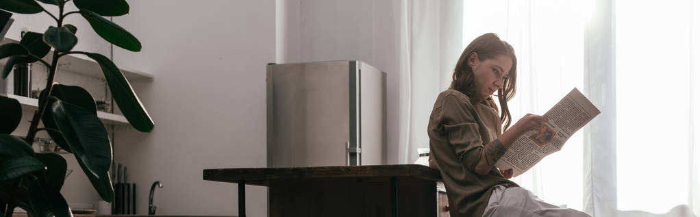 Πλευρική άποψη της γυναίκας με πόδι προσθετική ανάγνωση εφημερίδα στην κουζίνα, πανοραμική βολή - Φωτογραφία, εικόνα