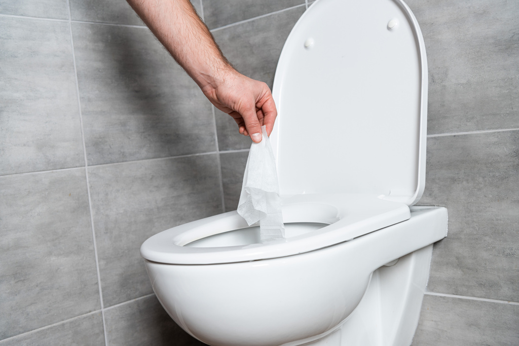 Ausgeschnittene Ansicht eines Mannes, der Serviette in weiße Toilettenschüssel im Badezimmer legt - Foto, Bild