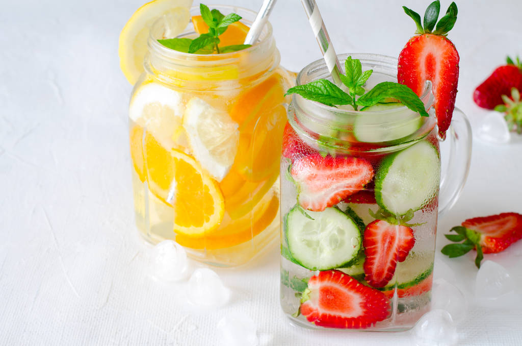 Bebidas geladas refrescantes de verão com laranja, limão, pepino e morango no fundo branco
 - Foto, Imagem