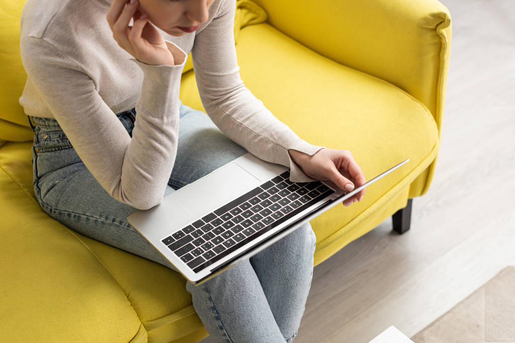 Обрезанный вид на девушку с помощью ноутбука на диване дома
 - Фото, изображение