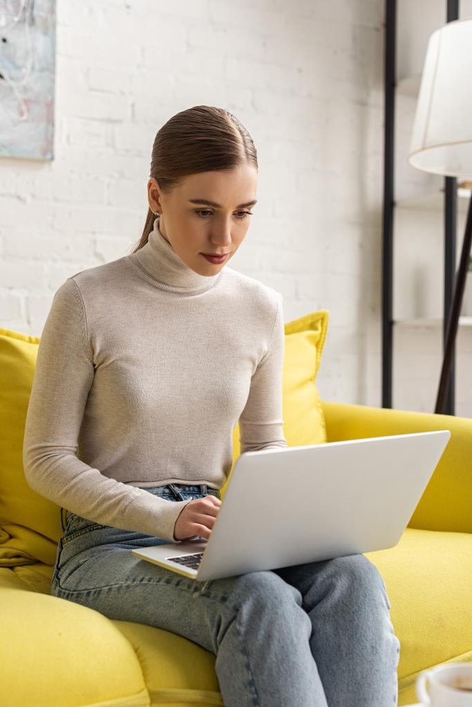 Freelancer atraente trabalhando no laptop no sofá na sala de estar
  - Foto, Imagem