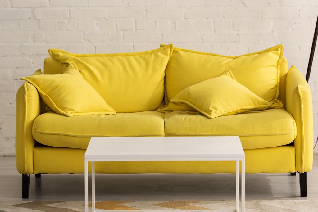 Жовтий диван з подушками та білим журнальним столиком у вітальні
 - Фото, зображення