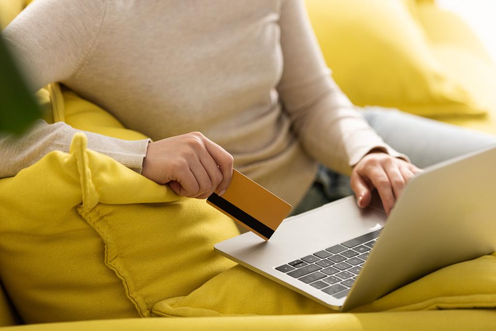 Gewassen weergave van de vrouw met behulp van laptop en met een creditcard op de bank  - Foto, afbeelding