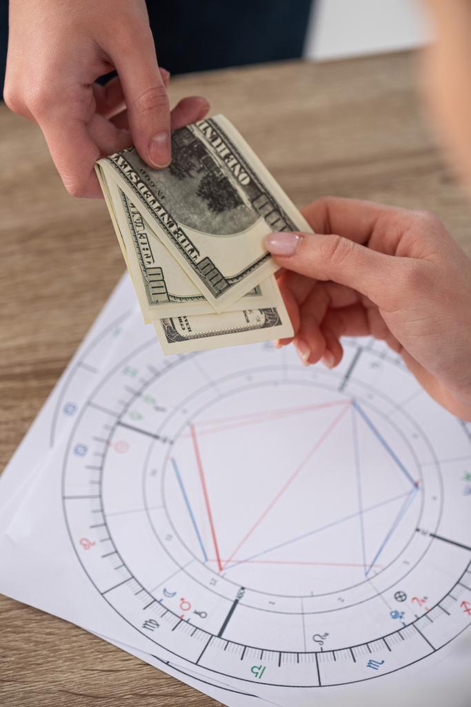 Ausgeschnittene Ansicht eines Mannes, der Astrologin neben Geburtshoroskopen auf dem Tisch Bargeld gibt - Foto, Bild