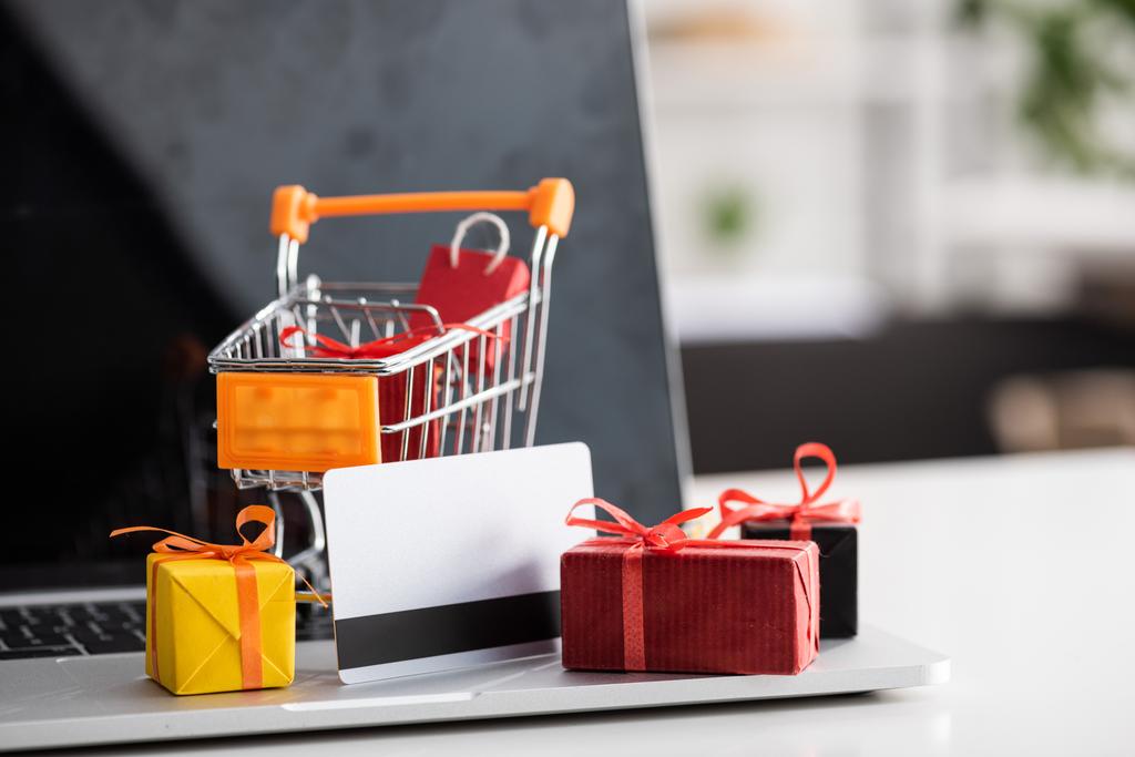 Selective focus of toy cart and gift boxes with credit card on laptop on table - 写真・画像