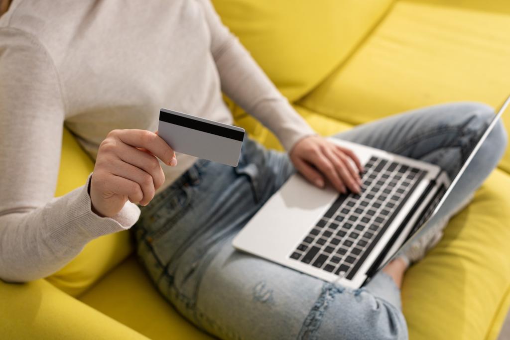 Widok kobiety trzymającej kartę kredytową i korzystającej z laptopa na kanapie - Zdjęcie, obraz
