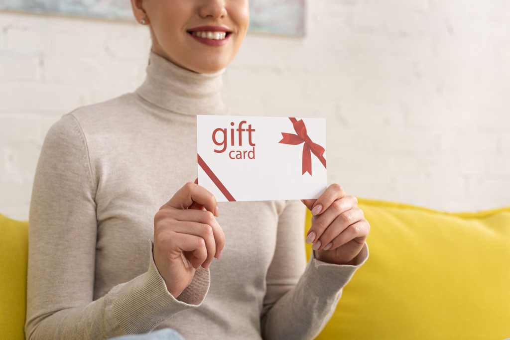 Widok na uśmiechniętą kobietę pokazującą kartę podarunkową na kanapie - Zdjęcie, obraz