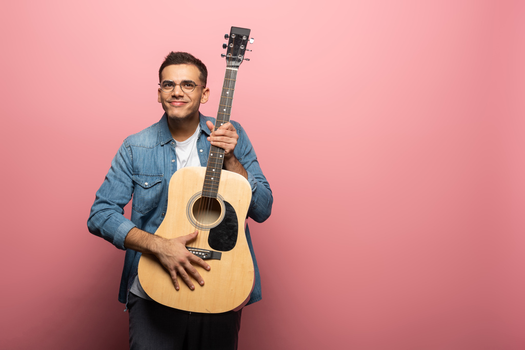 Mężczyzna uśmiecha się do kamery i trzyma gitarę akustyczną na różowym tle - Zdjęcie, obraz