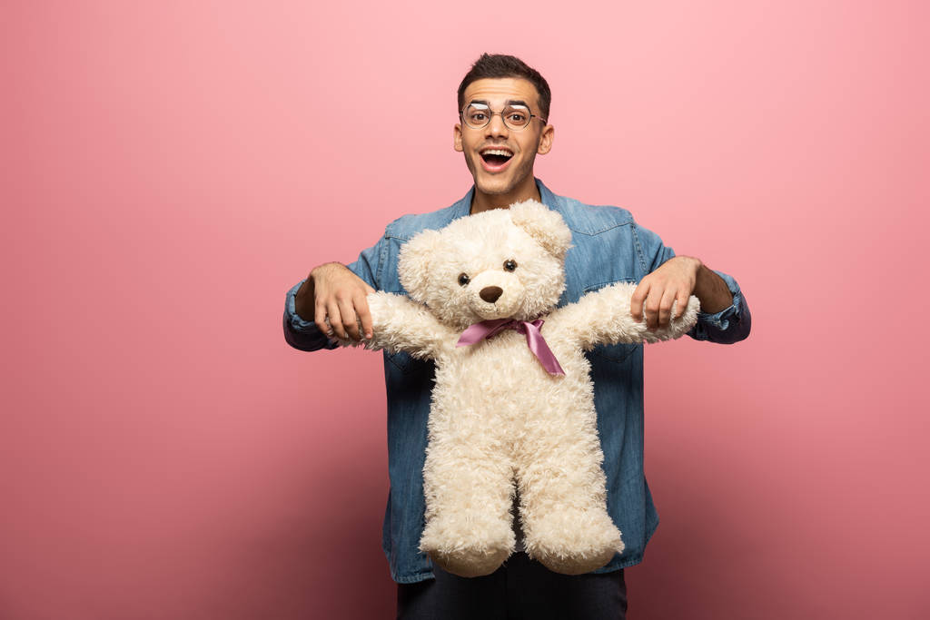 Surprised man with teddy bear looking at camera on pink background - Photo, Image