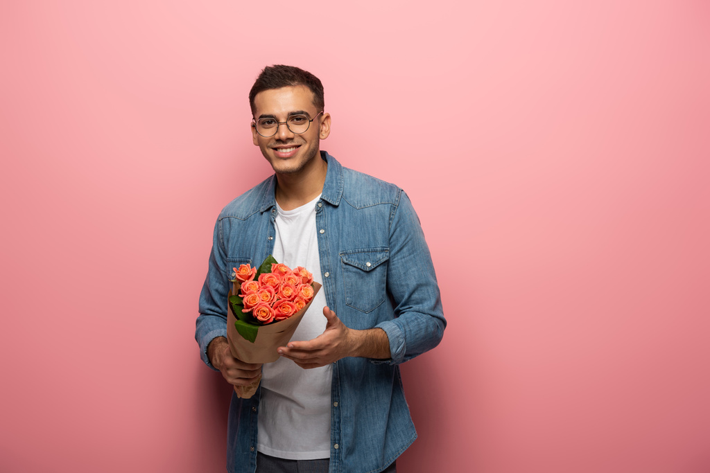 Young man with rose flowers smiling at camera on pink background - Photo, Image