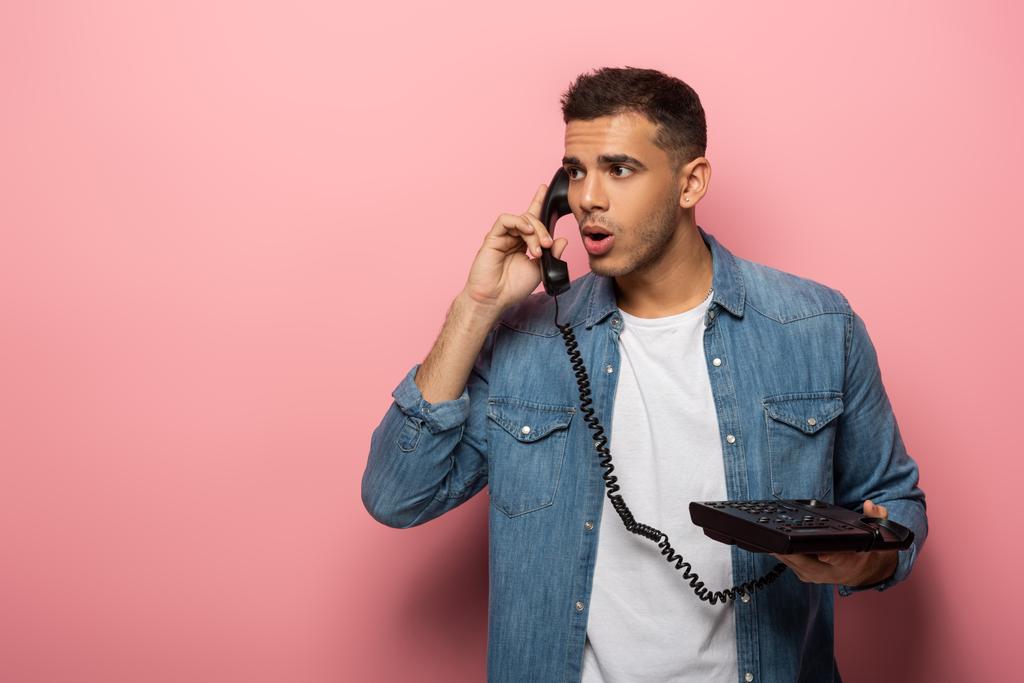 Excited man talking on telephone and looking away on pink background - Photo, Image