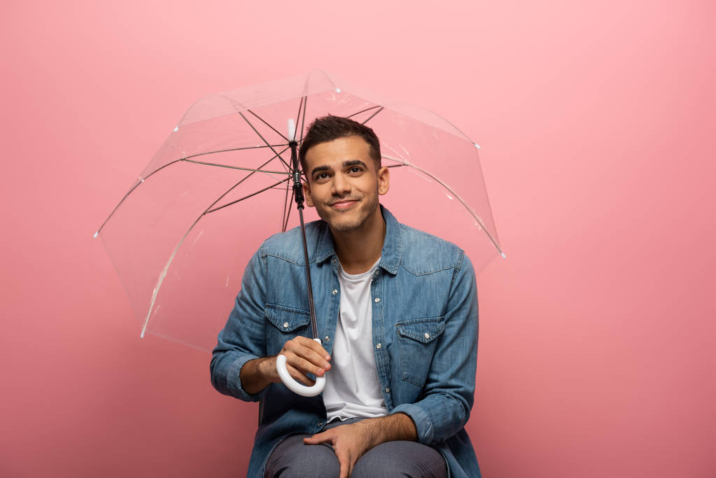 Lächelnder Mann mit durchsichtigem Regenschirm auf rosa Hintergrund - Foto, Bild