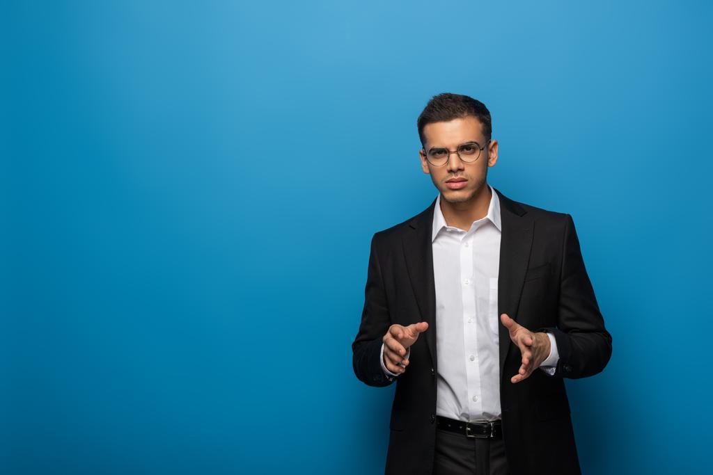 Jonge zakenman toont iets met handen op blauwe achtergrond - Foto, afbeelding