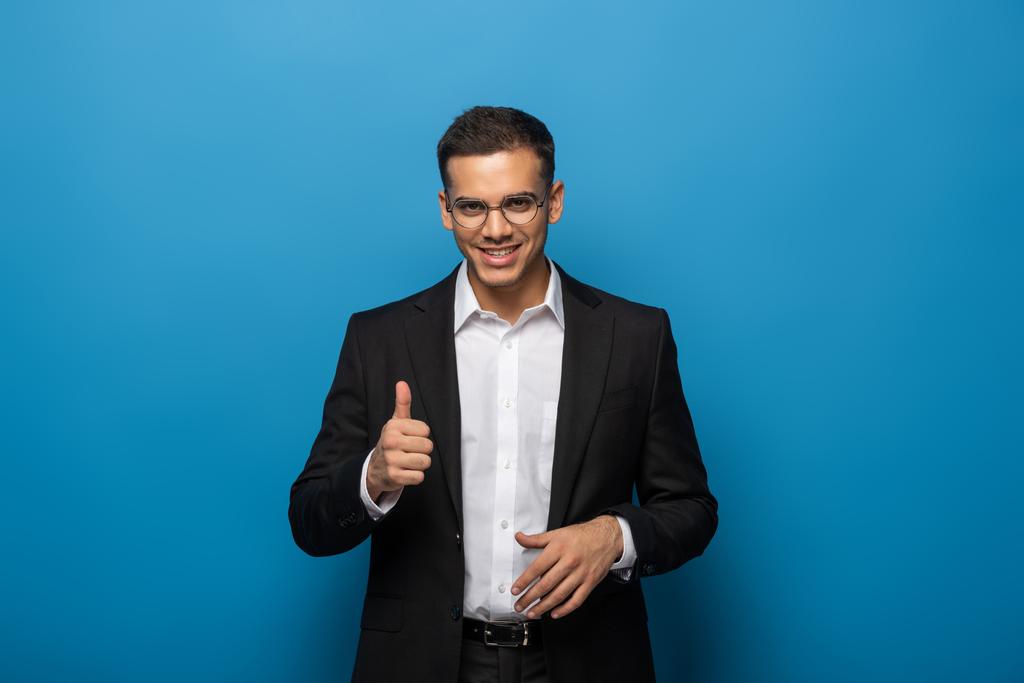 Улыбающийся бизнесмен показывает большой палец вверх жестом на синем фоне
 - Фото, изображение