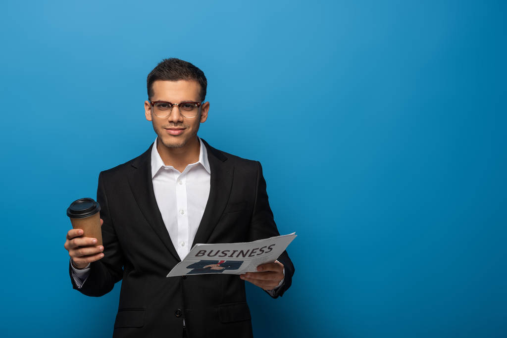 Όμορφος επιχειρηματίας κρατώντας εφημερίδα και κύπελλο μιας χρήσης σε μπλε φόντο - Φωτογραφία, εικόνα