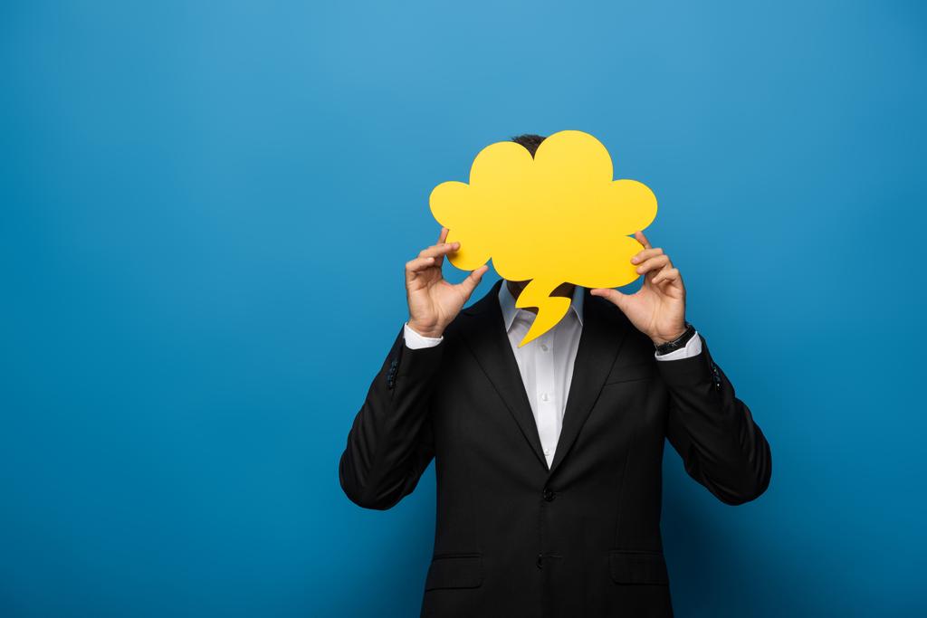 Businessman covering face with speech bubble on blue background - Photo, Image