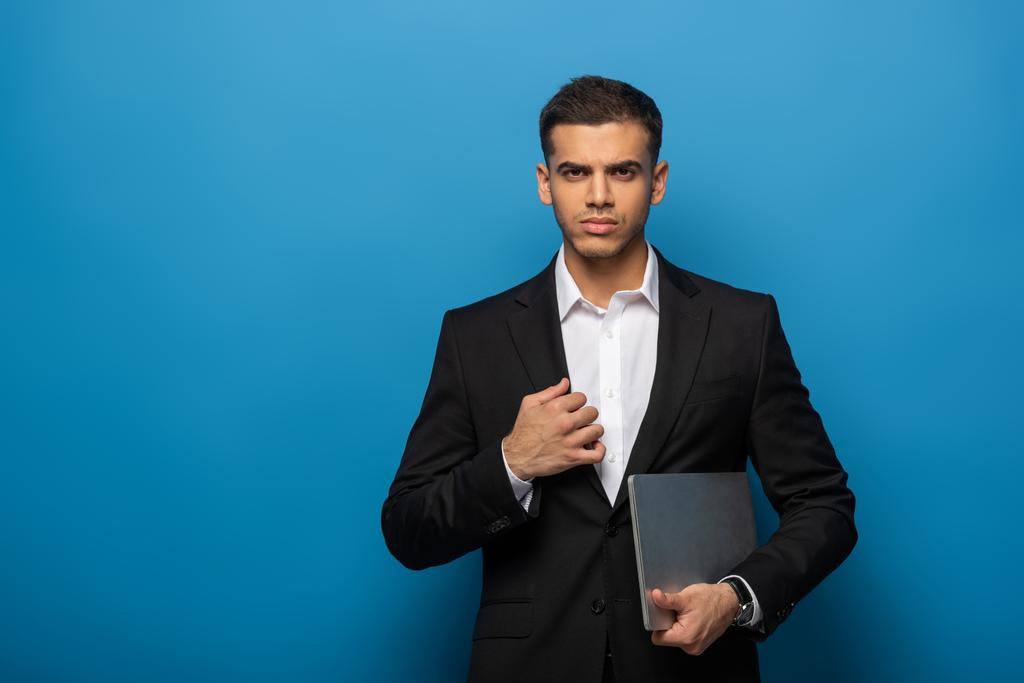 Handsome businessman with laptop looking at camera on blue background - Photo, Image