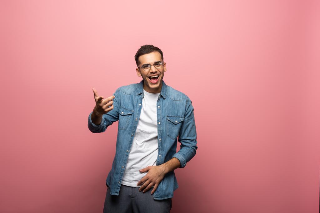 Веселый молодой человек, указывающий пальцем на камеру на розовом фоне
 - Фото, изображение