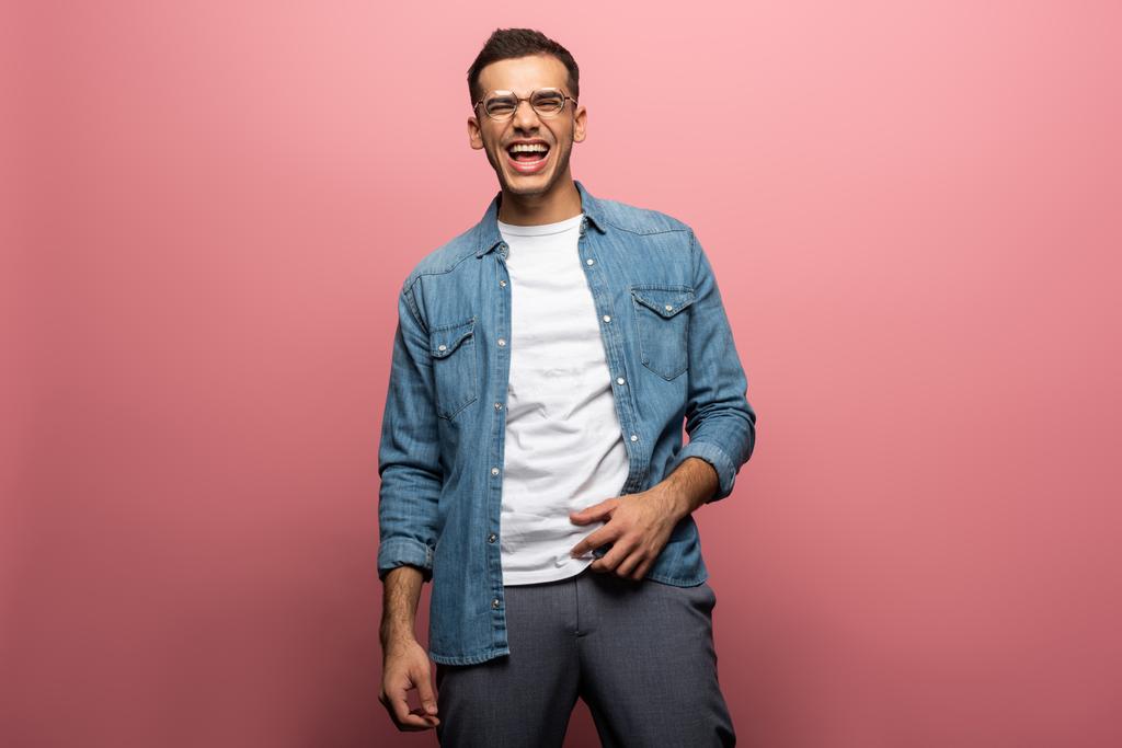 Knappe jongeman in bril lachend op roze achtergrond - Foto, afbeelding