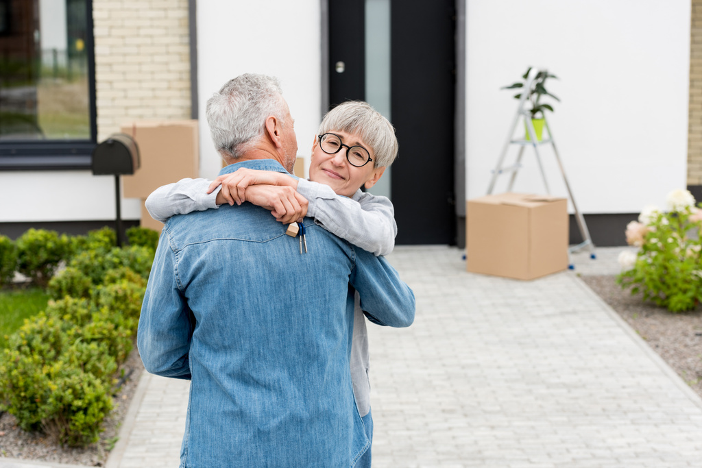 Lächelnde Frau hält Schlüssel für neues Haus und umarmt reifen Mann  - Foto, Bild