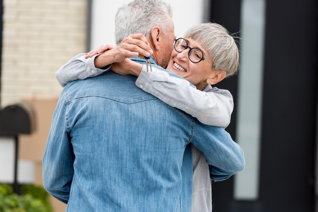 улыбающаяся женщина держит ключи от нового дома и обнимает зрелого мужчину
  - Фото, изображение