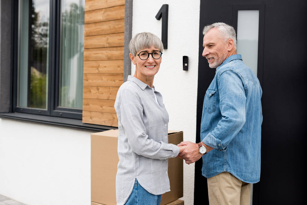 Älterer Mann blickt lächelnde Frau an und hält Händchen mit ihrem neuen Haus  - Foto, Bild