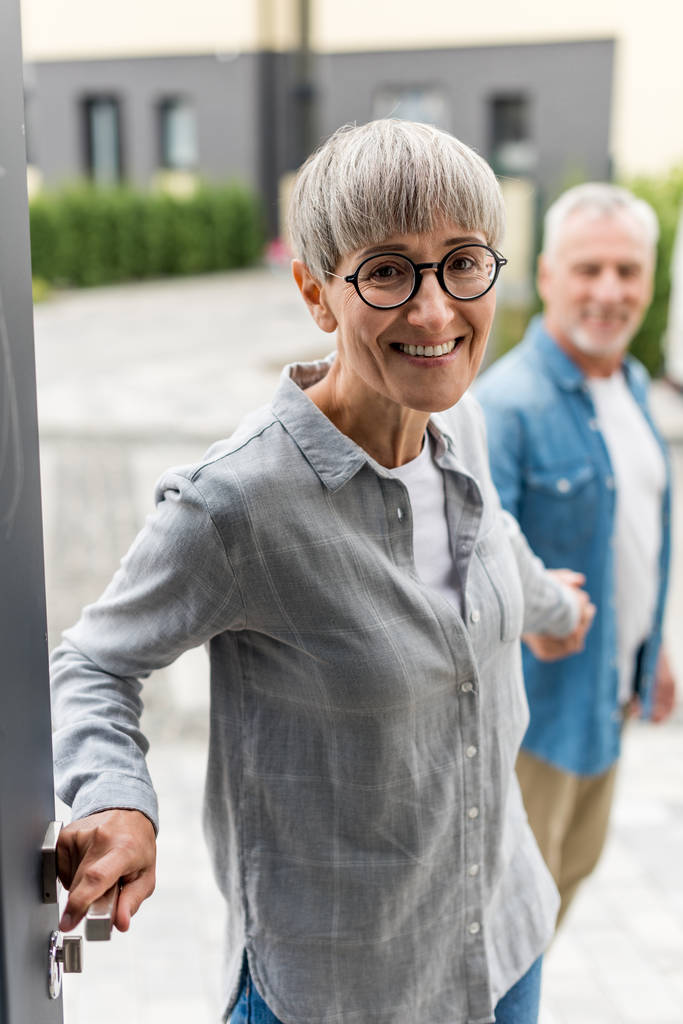 selective focus of smiling woman holding hands with man and entering to new house  - Photo, Image