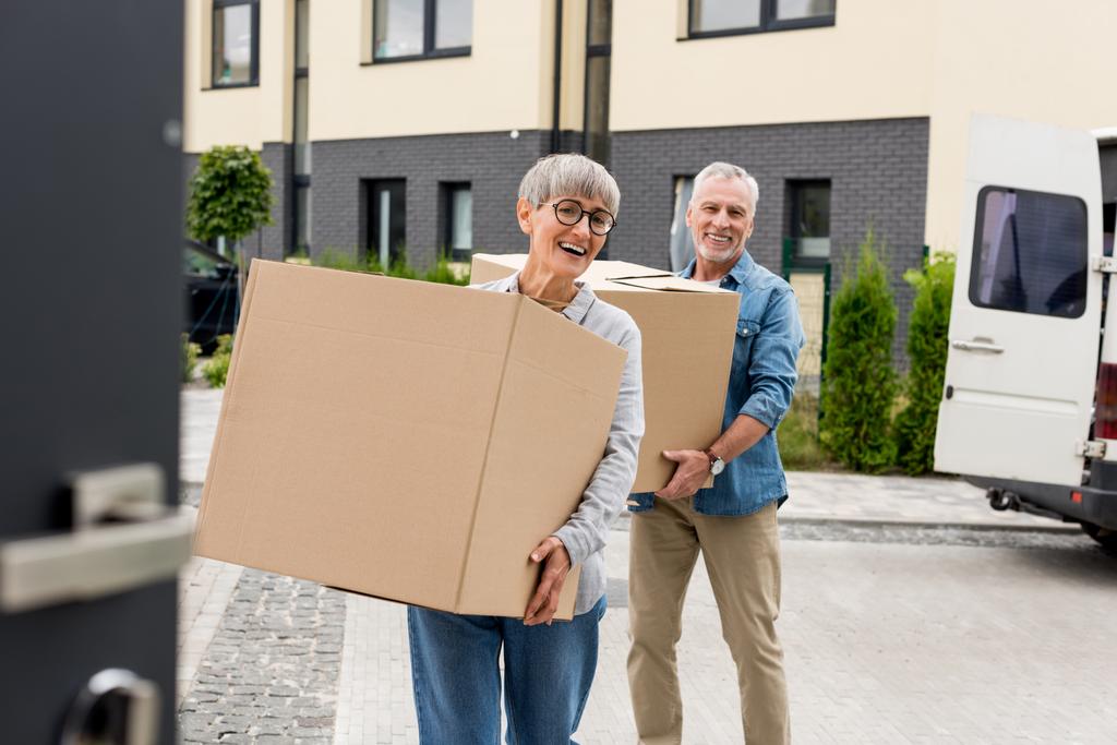 mature man and smiling woman bringing boxes to new house  - Photo, Image