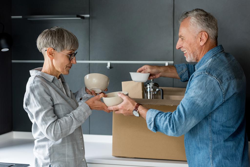 glimlachende man en volwassen vrouw uitpakken doos in nieuw huis  - Foto, afbeelding