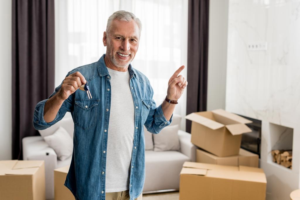 улыбчивый мужчина, держащий ключи и указывающий пальцем на новый дом
  - Фото, изображение