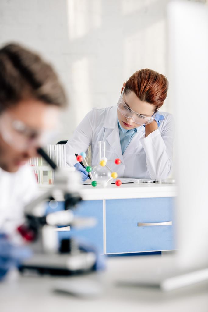selective focus of genetic consultant writing and colleague using microscope in lab  - 写真・画像