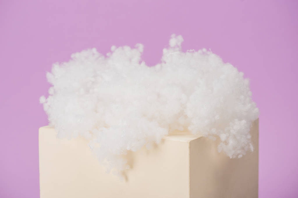 witte pluizige wolk van katoenen wol op kubus geïsoleerd op violette achtergrond - Foto, afbeelding