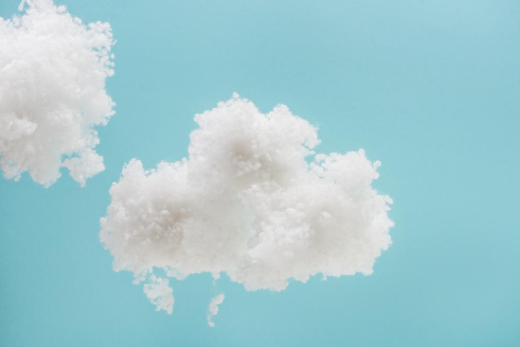 青い背景に隔離されたコットンウールで作られた白いふわふわの雲 - 写真・画像