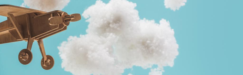 wooden toy plane flying among white fluffy clouds made of cotton wool isolated on blue, panoramic shot - Photo, Image