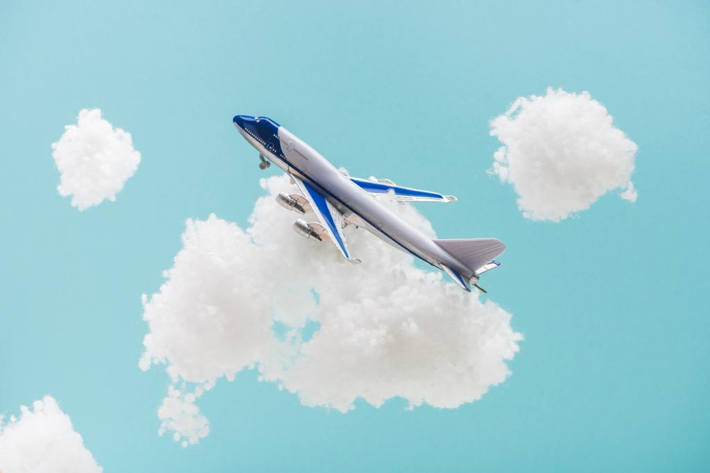 speelgoedvliegtuig vliegen tussen witte pluizige wolken van katoen wol geïsoleerd op blauw - Foto, afbeelding